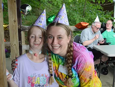 A camper and counselor wearing party hats
